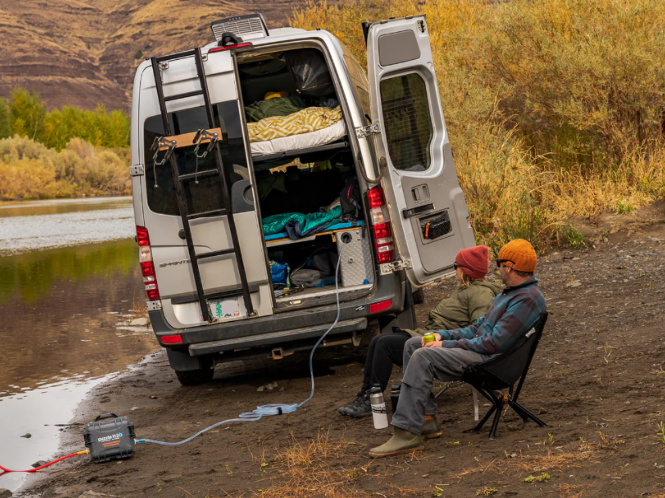 People using a water purifier in a river outside a camper van