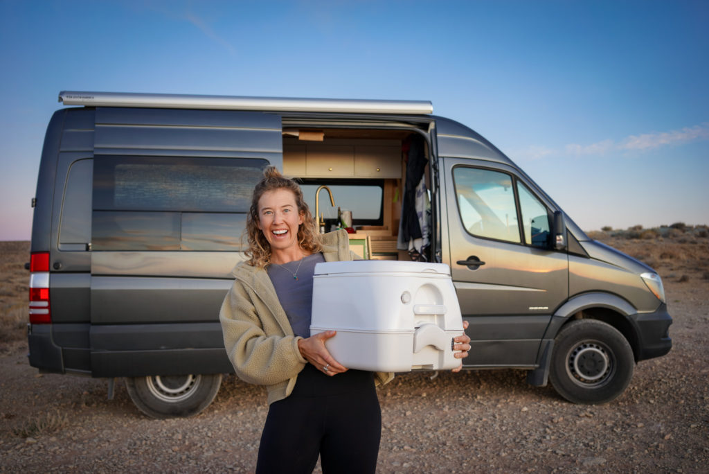 Person holding a portable toilet in front of a camper van