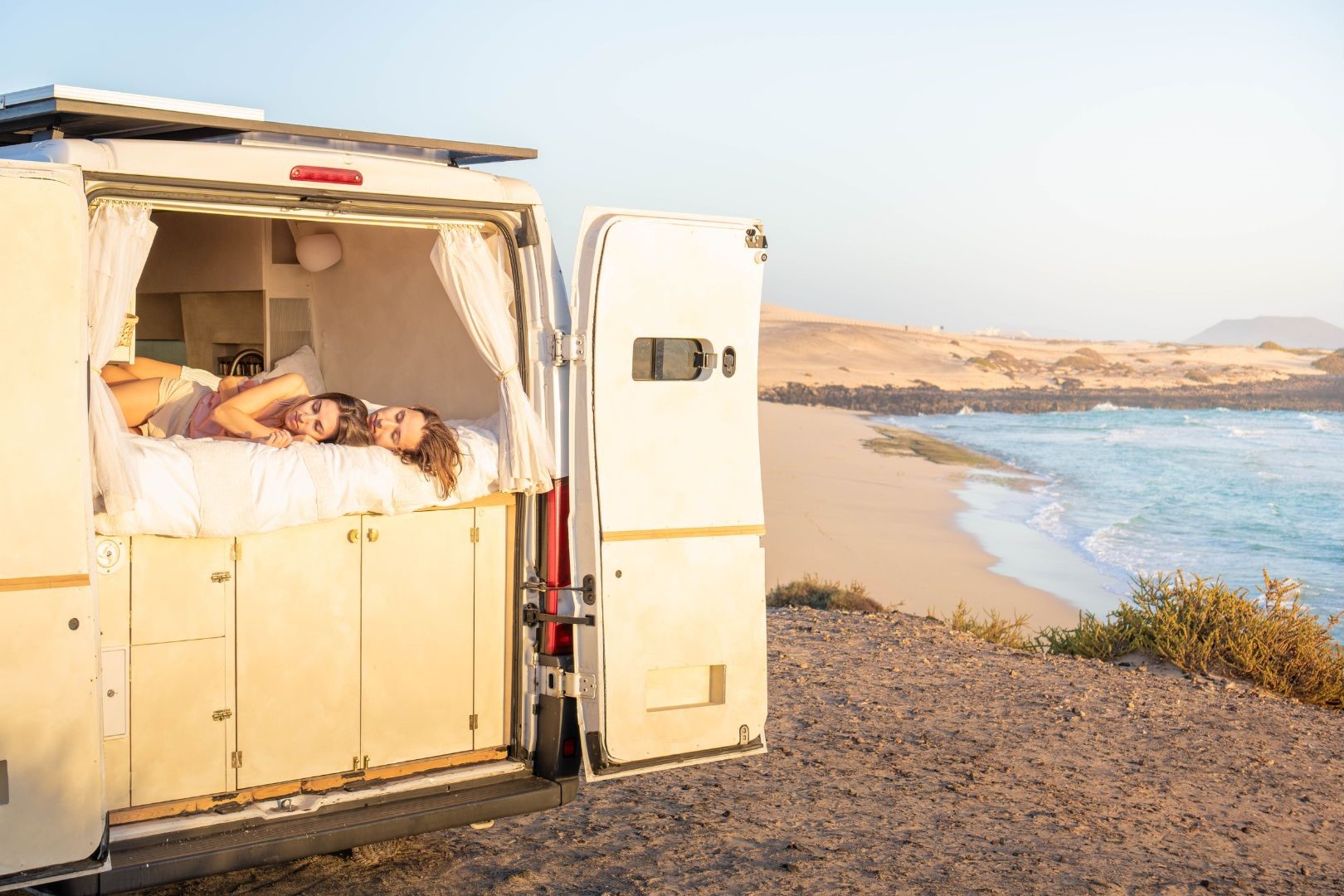 People in campervan bed at beach